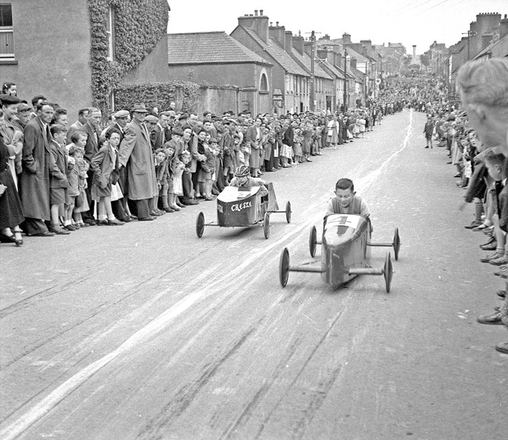 1_cropped-(1).JPG black and white photograph showing two soap box cars racing down a street with crowds watching from the sides.